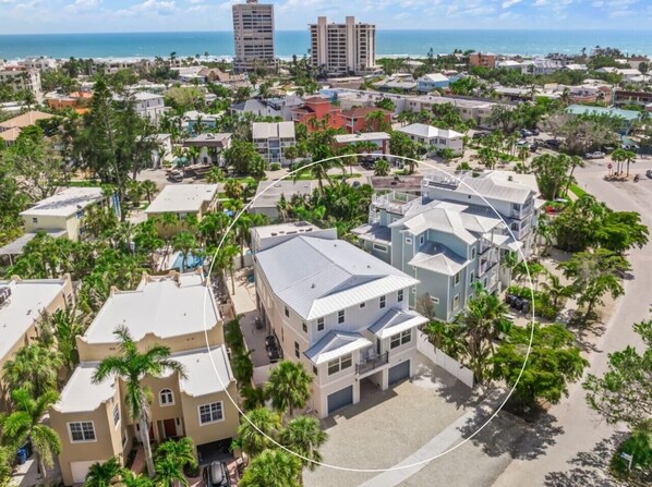 Zona residencial con edificios de diferentes alturas, rodeada de vegetación y una playa al fondo.
