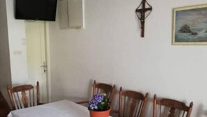 A dining area with a long table, chairs, a potted plant, a wall-mounted TV, and a door. - Holiday Home Ribarić (Rab)