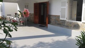 A covered outdoor area with a table and chairs, a wooden door, and a window with shutters. - Holiday Home Ribarić (Rab)