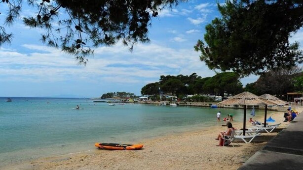 A beach with clear water, umbrellas, and people. - Holiday Home Ribarić (Rab)