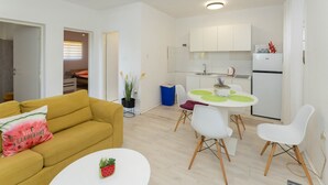 Un appartement moderne avec un canapé jaune, une table à manger et quatre chaises, un coin cuisine et un petit balcon.