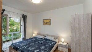 Une chambre à coucher comprenant un lit, deux tables de chevet, une commode, une fenêtre avec des rideaux, un luminaire au plafond et un tableau accroché au mur.