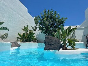 A clear blue pool surrounded by white walls and tropical plants. - Natural Zen Rebirth (Corralejo)