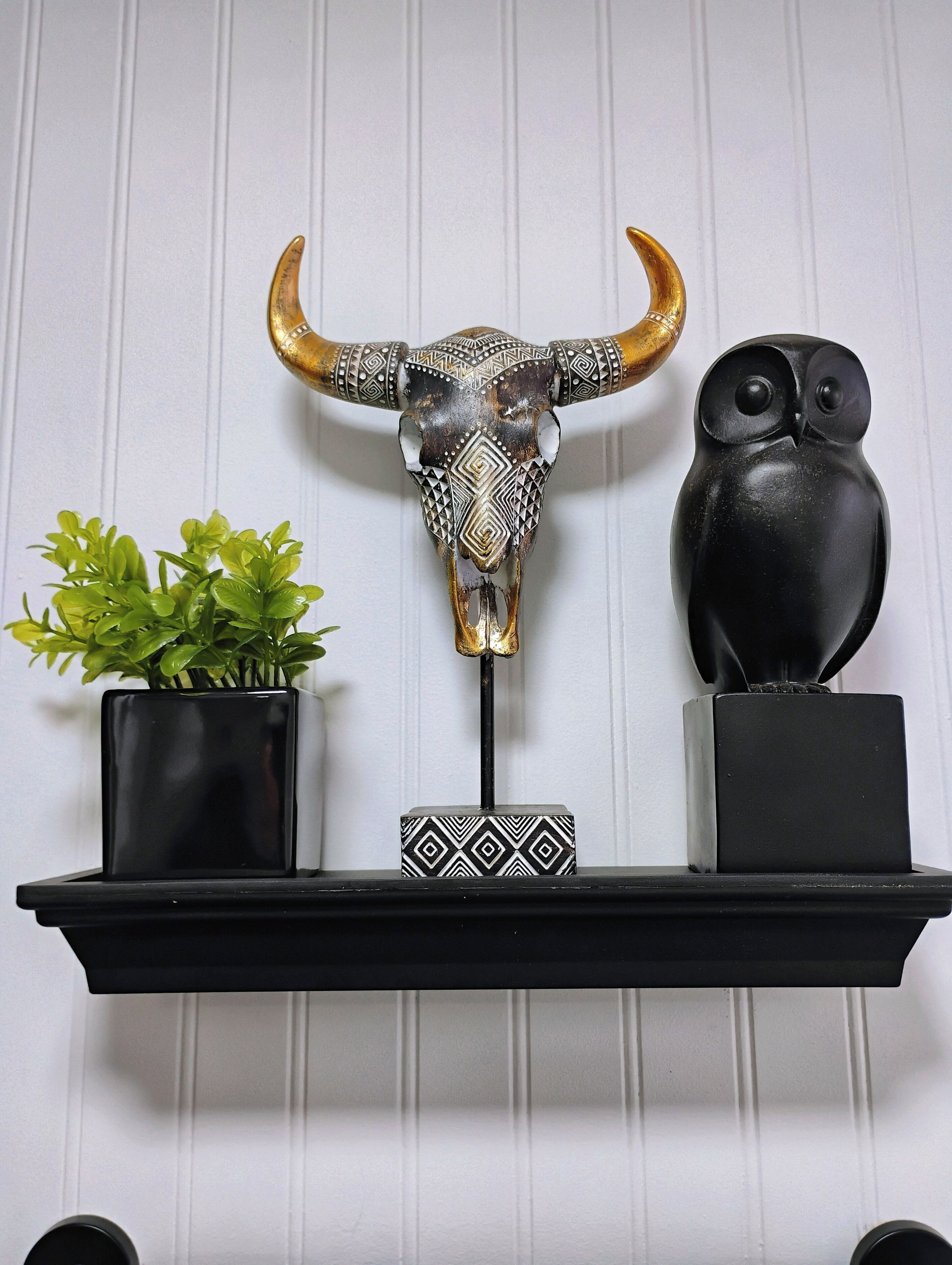 Une étagère ornée d’un crâne de taureau décoratif, d’une statuette de hibou noire et d’une petite plante en pot.