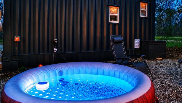 A hot tub in front of a building with a window and a chair. - Cozy Container, HotTub, King Bed, Pets, Wifi, 1 Night Stays, Griddle, Firepit (Chillicothe)