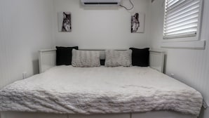 A bedroom with a white bed, two black pillows, a white radiator, and two wall-mounted air conditioning units. - Cozy Container, HotTub, King Bed, Pets, Wifi, 1 Night Stays, Griddle, Firepit (Chillicothe)