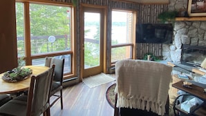 Un interior acogedor con chimenea de piedra, techo de madera y grandes ventanas que ofrecen vistas al verdor exterior.