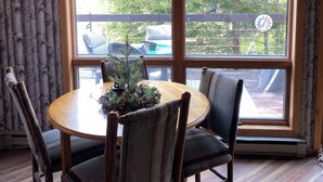 Comedor con mesa y sillas de madera, una planta decorativa y un amplio ventanal con vistas a árboles y una terraza.