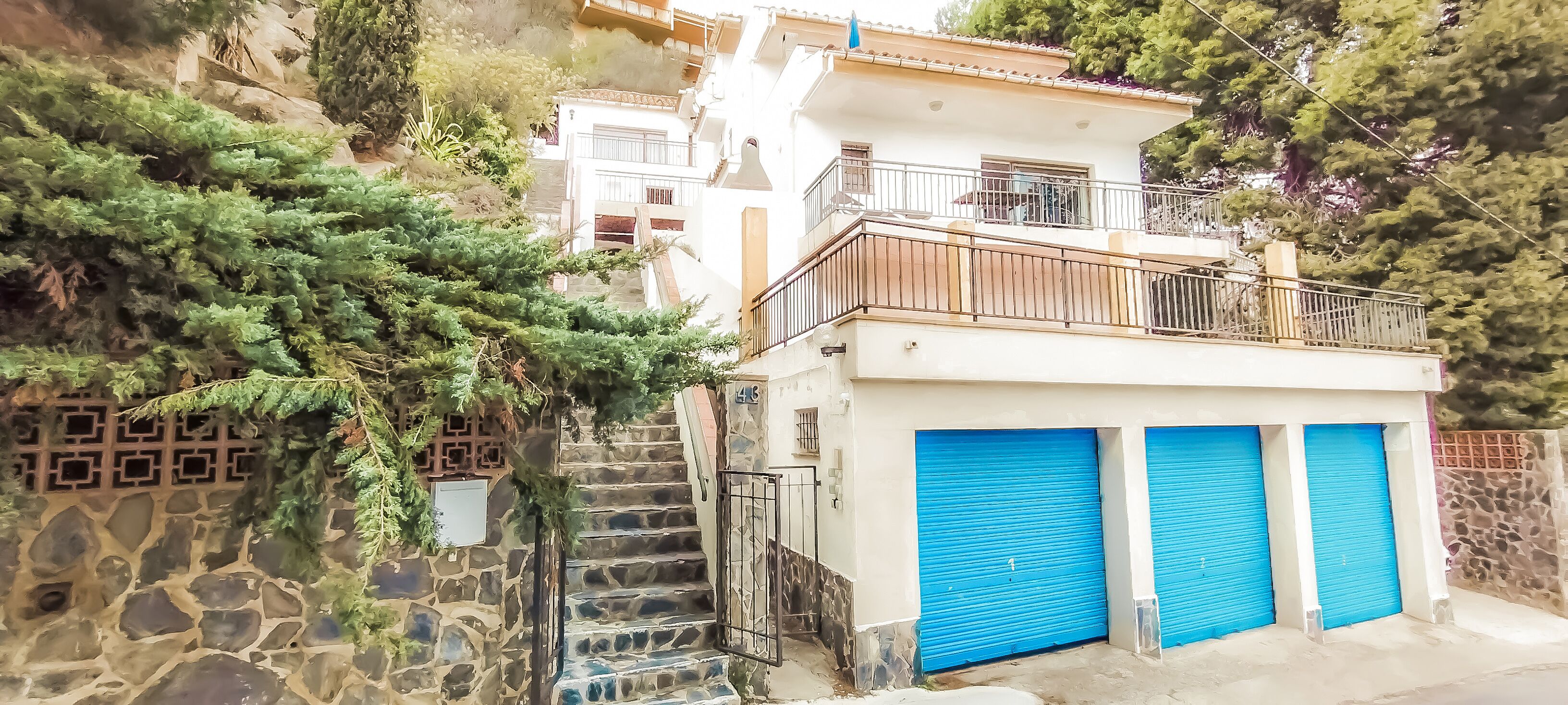 A building with a stone staircase, a balcony, and blue garage doors.