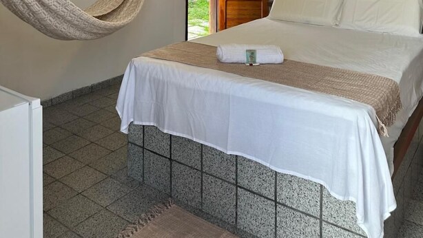 Een hotelkamer met een bed, een hangstoel, een houten deur en uitzicht op de natuur.