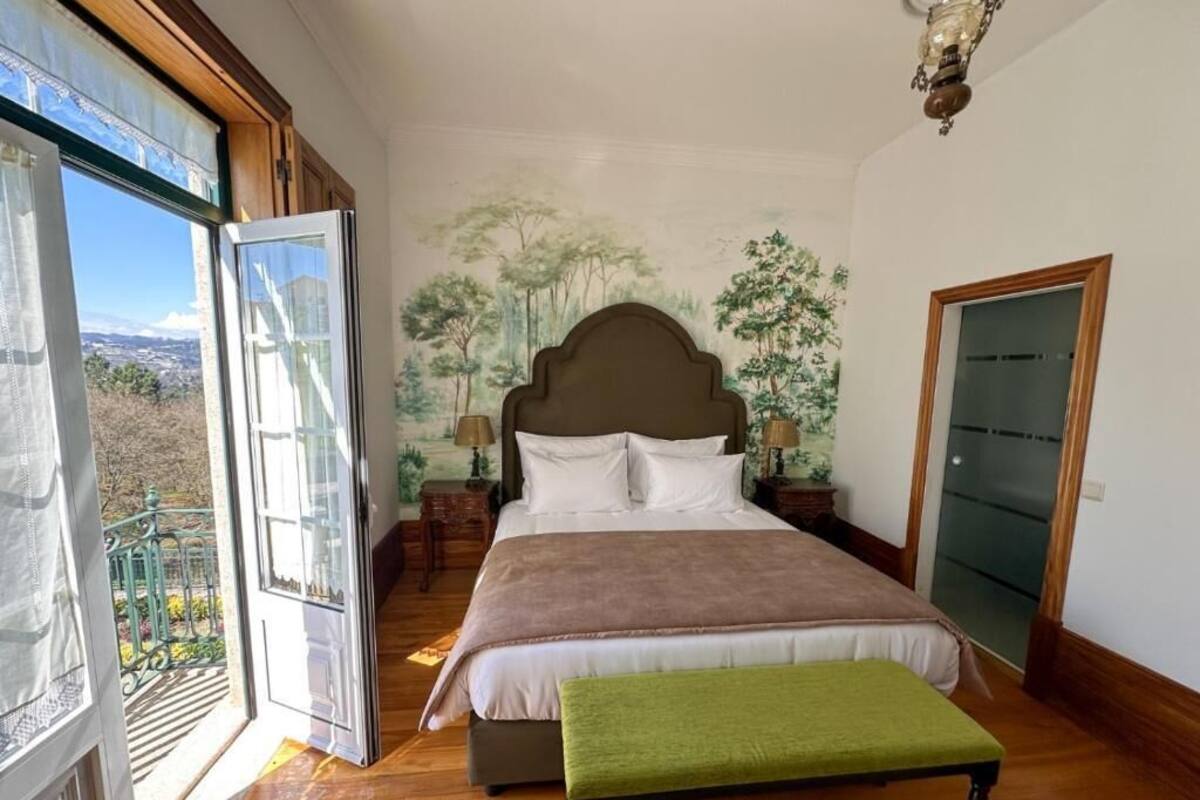 A bedroom with a large bed, a bench, a nightstand with a lamp, and a door.