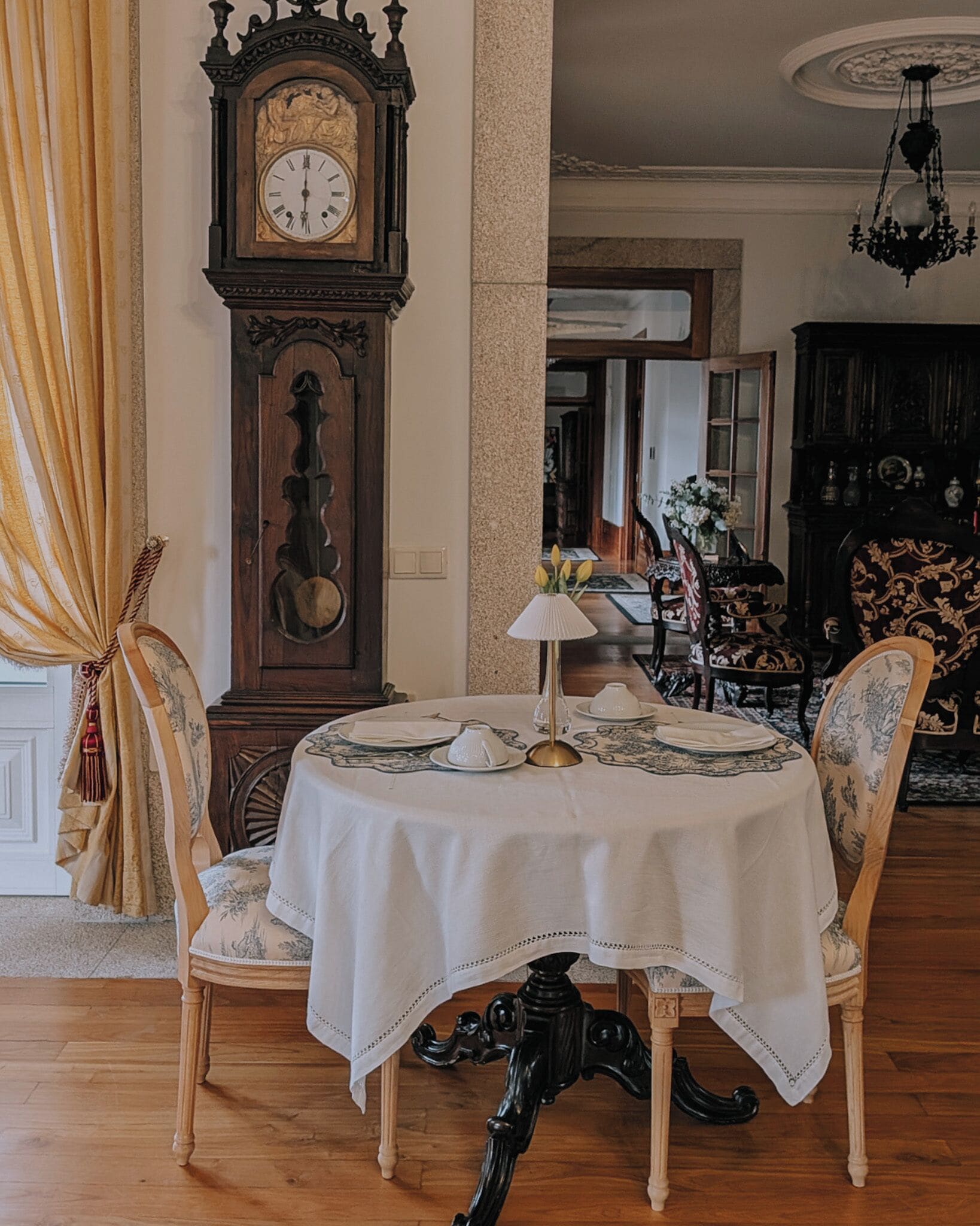 Un comedor con una mesa redonda, sillas, un reloj y una araña.