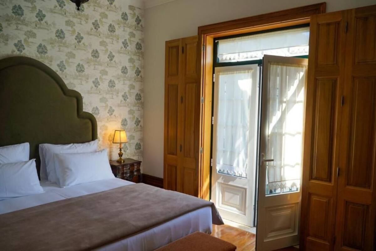 A bedroom with a bed, a nightstand with a lamp, a wooden wardrobe, and a door leading to a balcony.