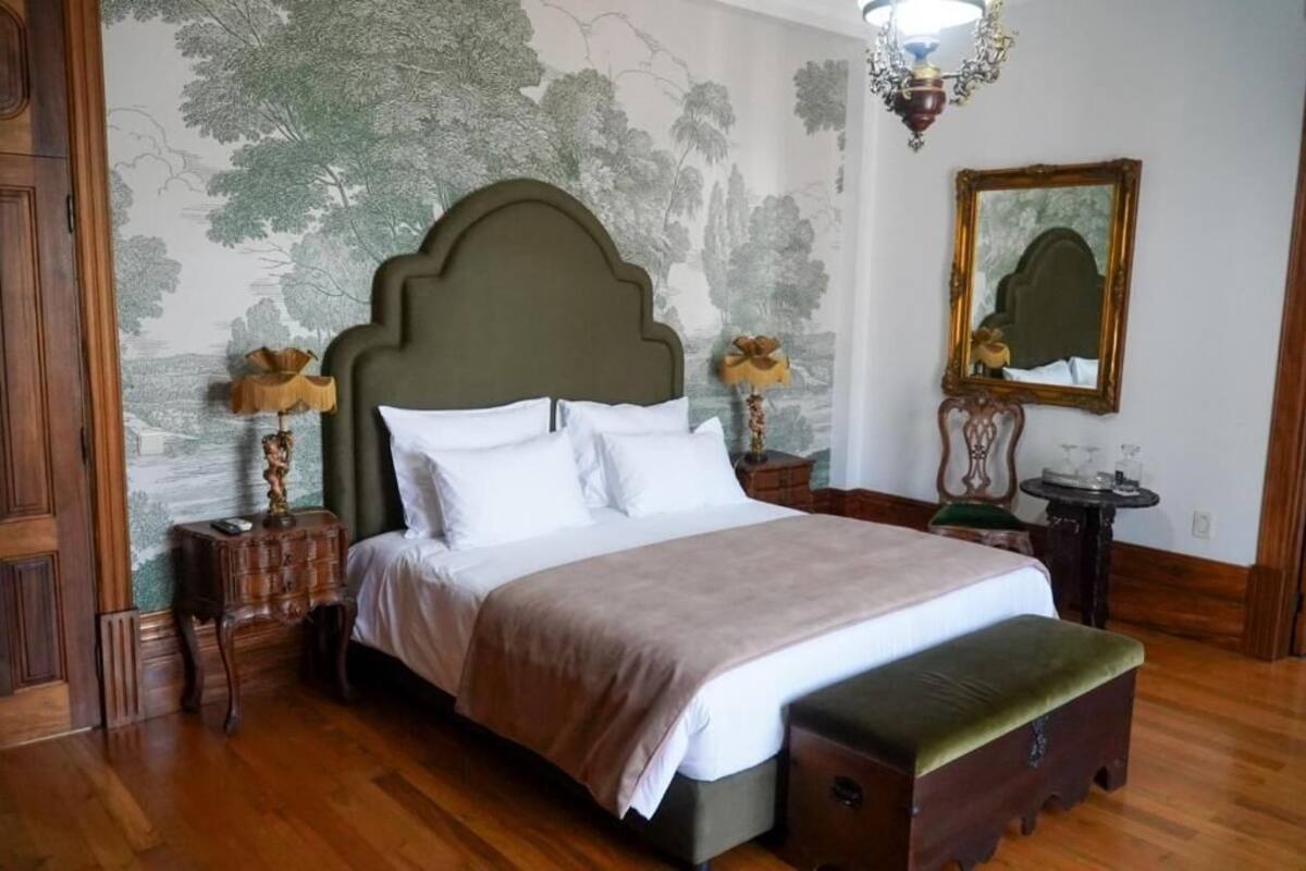 A neatly arranged bedroom with a large bed, a bench, a dresser, and a mirror on the wall.