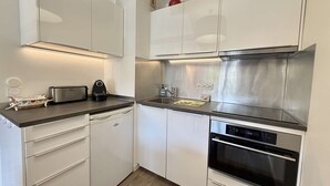 Une cuisine compacte avec des meubles blancs, une hotte de cuisinière en acier inoxydable, un four encastré et un plan de travail sur lequel se trouvent un grille-pain et une bouilloire.