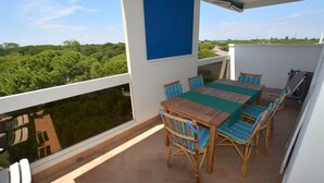 A balcony with a table and chairs, a blue awning, and a view of greenery.