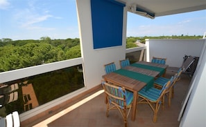 Un balcon avec une table et des chaises, un auvent bleu et une vue sur la verdure.