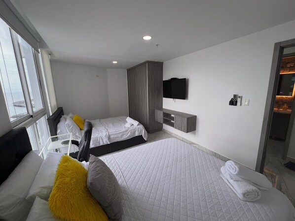 A modern hotel room with two beds, a TV, and a bathroom visible through an open door.