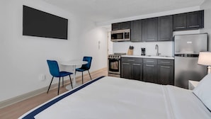 A compact hotel room with a bed, a small dining table with chairs, a kitchenette with a microwave, stove, and refrigerator, and a TV mounted on the wall. - One Block to the Boardwalk! (Seaside Heights)