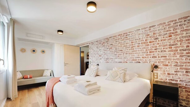 Une chambre à coucher moderne avec un grand lit, un mur décoré d’un motif en briques et une cheminée intégrée.