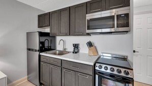 Una cocina compacta con gabinetes oscuros, un refrigerador de acero inoxidable, un microondas, un fregadero y una estufa.