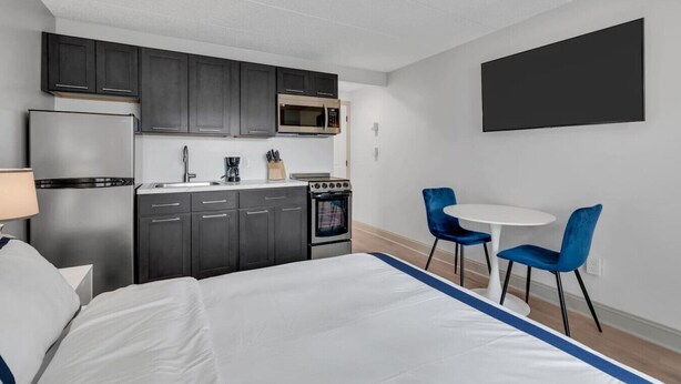Una habitación de hotel moderna con kitchenette, una cama, un televisor y dos sillas azules.