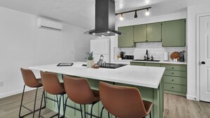 A modern kitchen with a white island, green cabinets, and a stainless steel range hood.