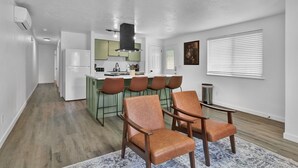 A modern kitchen with a central island, bar stools, and a seating area with leather chairs.