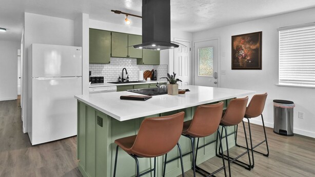 A modern kitchen with a central island, bar stools, a stainless steel trash can, and a painting on the wall.