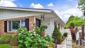 A two-story house with a brick facade, a front porch, and a well-maintained garden with roses.