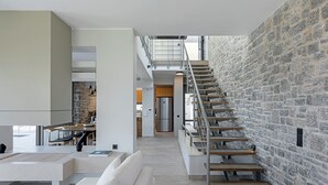 A modern interior with a staircase against a stone wall, a dining area, and a kitchen visible in the background. - Design villa with immaculate views in Theologos (Theologos)