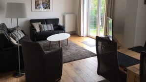 Una sala de estar moderna con un sofá de cuero negro, una mesa de centro blanca, una lámpara de pie y una zona de comedor con una mesa y sillas.