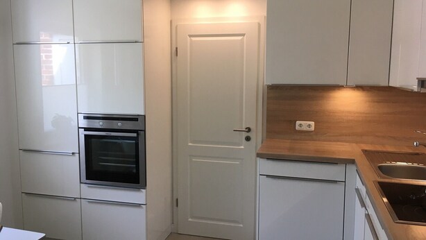 Una cocina compacta con armarios blancos, horno empotrado, encimera de madera y un lavabo.