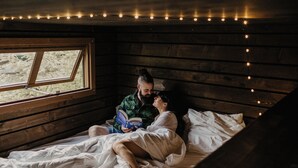 A cozy room with wooden walls, a window, and string lights. - Nutchel Cosy and Nature Cabin for 4 (Martelange)