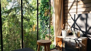 A cozy room with a large window, a wooden stool, a fireplace, and a bed. - Nutchel Cosy and Nature Cabin for 4 (Martelange)