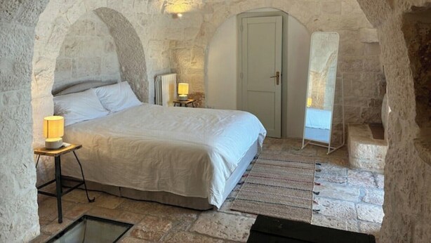 Une chambre à coucher avec un plafond en forme d’arc en pierre, un lit, une table de chevet avec une lampe et une porte.