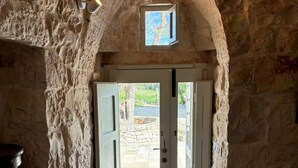 Un couloir aux murs de pierre, avec une porte en arc donnant sur un espace extérieur.