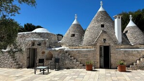 Il s’agit d’un bâtiment traditionnel en pierre, doté de toits coniques et d  ’un escalier en pierre menant à une porte. On peut y voir deux plantes en pot et deux chaises à l’extérieur.