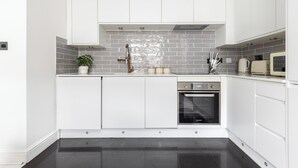 A modern kitchen with white cabinets, a tiled backsplash, a built-in oven, and a countertop with a kettle and utensils.