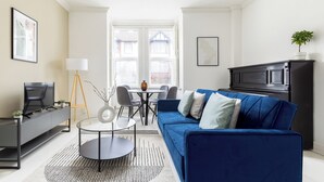 A modern living room with a blue sofa, a TV, and a dining area with a table and chairs.