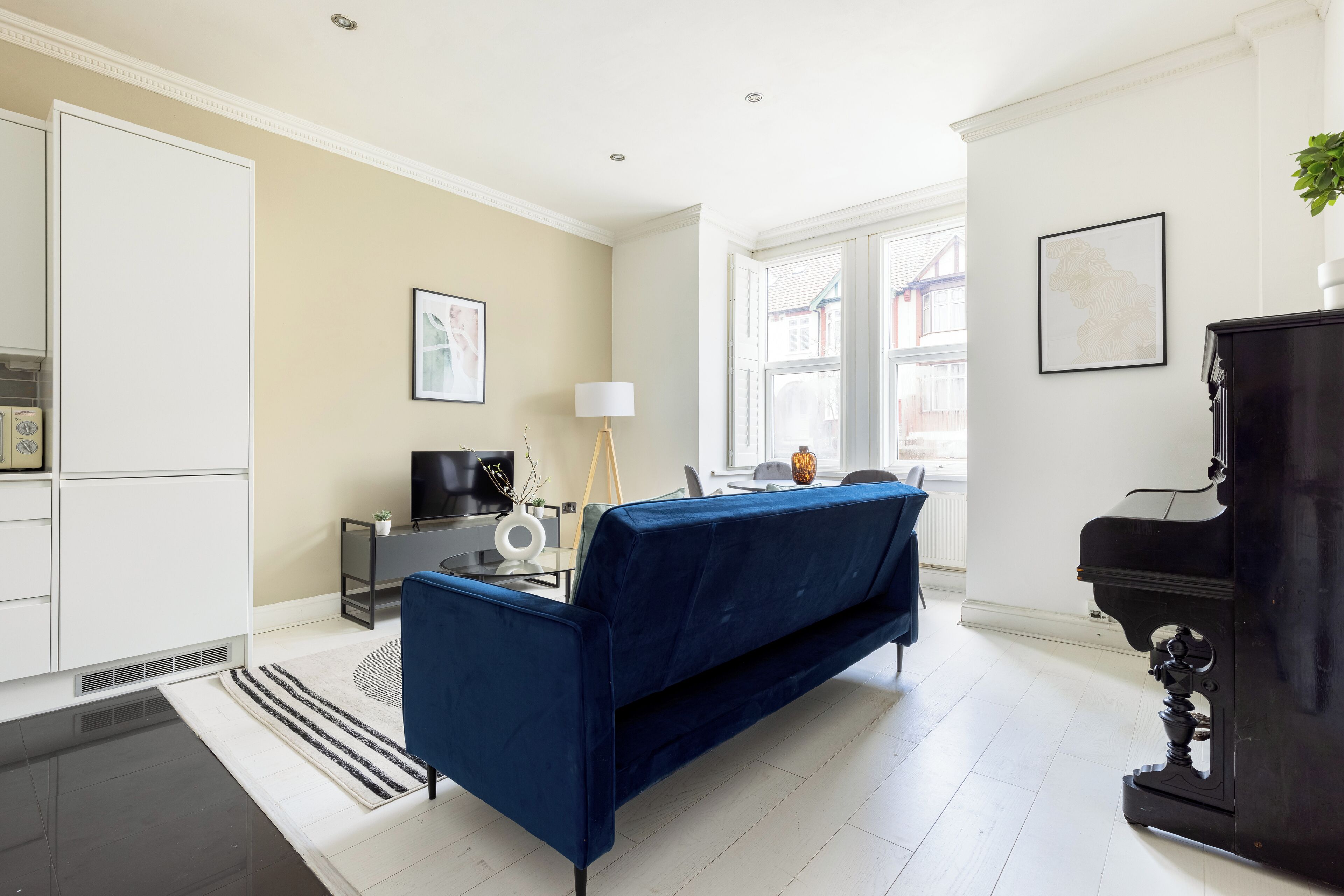 A modern living room with a blue sofa, a black piano, and a large window offering a view of the outside.
