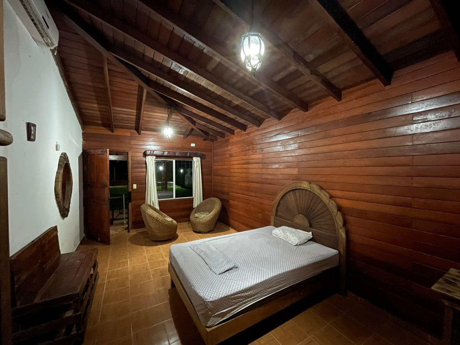 Una habitación con paneles de madera, una cama, dos sillas y un ventanal.