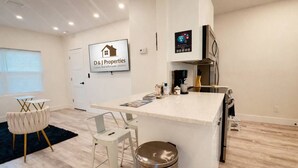 A modern kitchen with a central island, bar stools, a coffee machine, and a D & J Properties sign. - Daytona Double Delight (Daytona Beach)