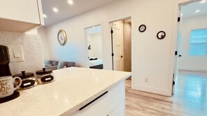 A kitchen with a countertop, a coffee maker, and jars. There is a clock on the wall and a door leading to another room. - Daytona Double Delight (Daytona Beach)