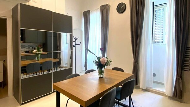 A modern dining area with a wooden table and chairs, a vase with flowers, and a partition with built-in shelves. - Casa Angelina - Cozy stay near the most beautiful destinations in Puglia (Molfetta)