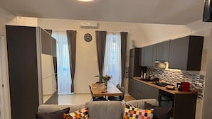 A modern living room with a grey sectional sofa, a dining table, and a kitchen area. - Casa Angelina - Cozy stay near the most beautiful destinations in Puglia (Molfetta)