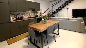 A modern kitchen with dark cabinets, a wooden dining table, and a staircase leading to an upper level. - Casa Angelina - Cozy stay near the most beautiful destinations in Puglia (Molfetta)