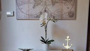 Ein weißes Schränkchen mit Schubladen und Regalen, ein Blumentopf, ein dekorativer Anker und eine Weltkarte an der Wand darüber.