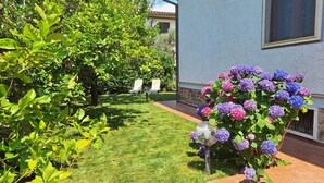Ein gepflegter Garten mit verschiedenen Pflanzen und Blumen, einem deutlichen Weg und einem Gebäude mit einer Steinaußenwand.