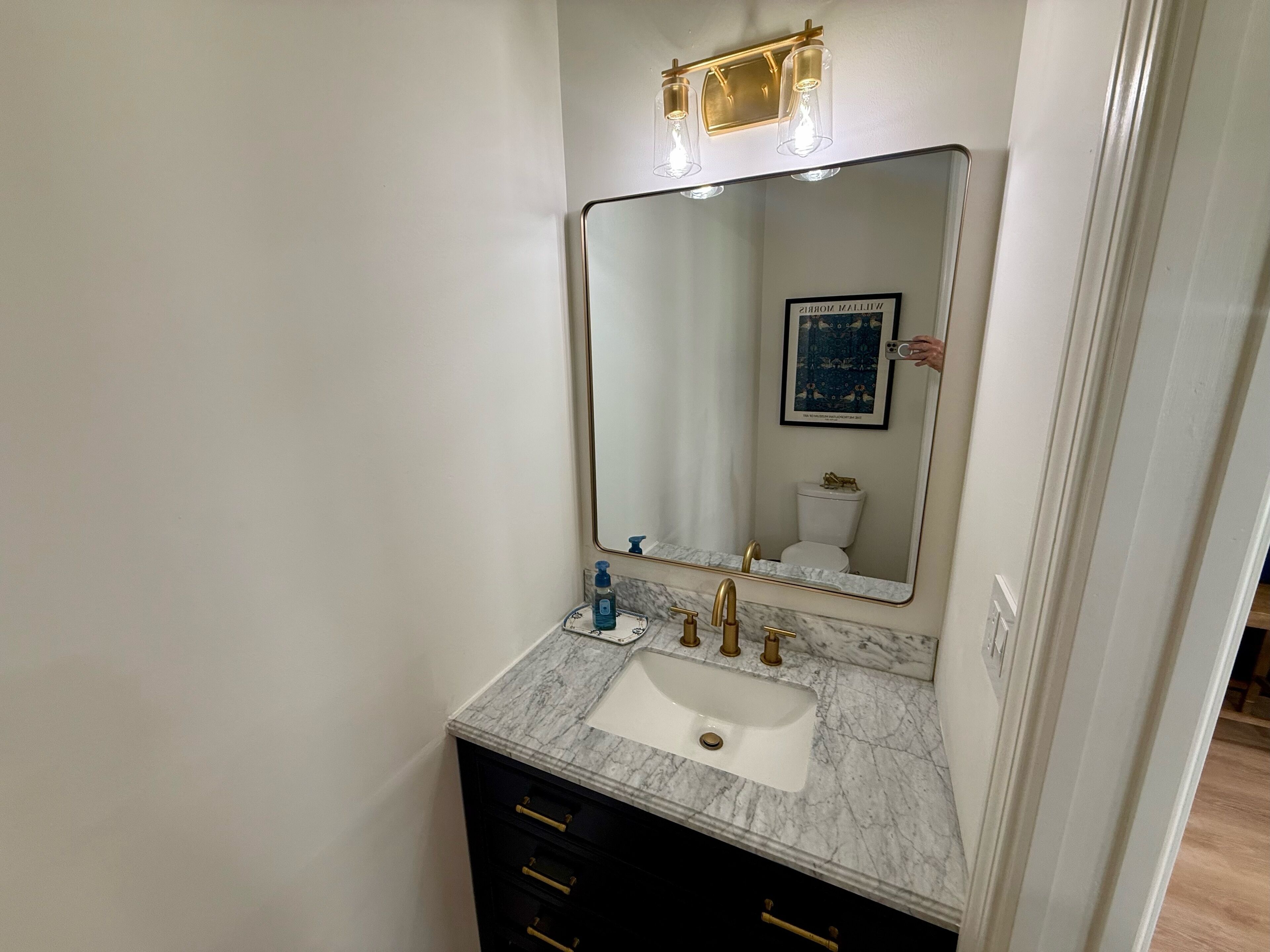 Un baño con lavamanos blanco, grifos dorados y un espejo grande.
